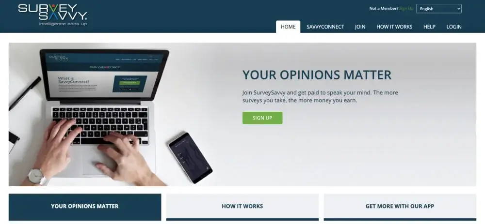 Survey Savvy Hero image featuring a title with a sign up button and an image with a person writing on the laptop and a celphone and pen on the desk