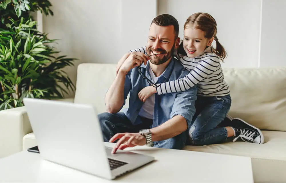 Father and daughter smiling while looking at a laptop screen.